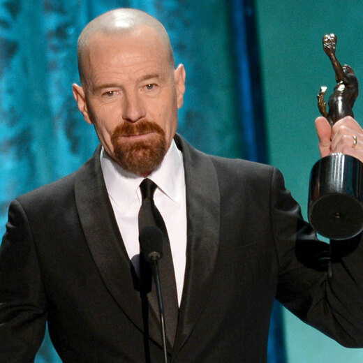 Actor Byran Cranston with a shaved head and he's holding an Emmy.