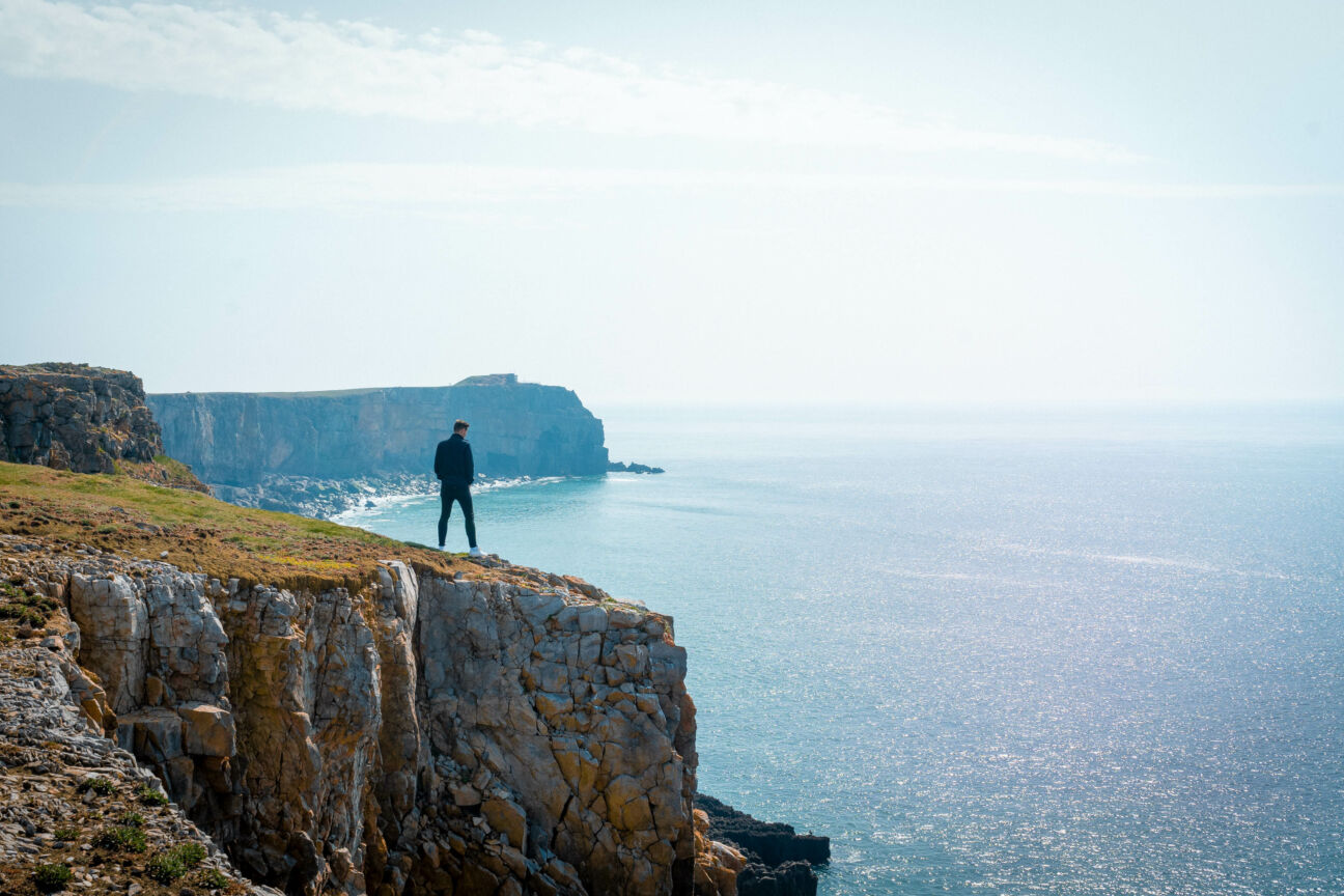 man looks over cliffs while coasteering
