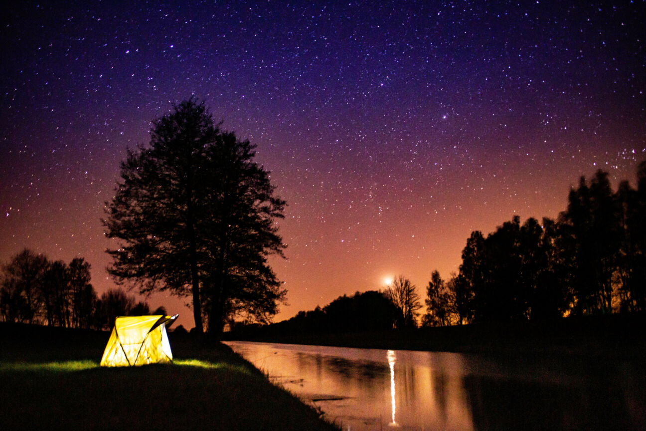 tent glows under stars and night sky while camping