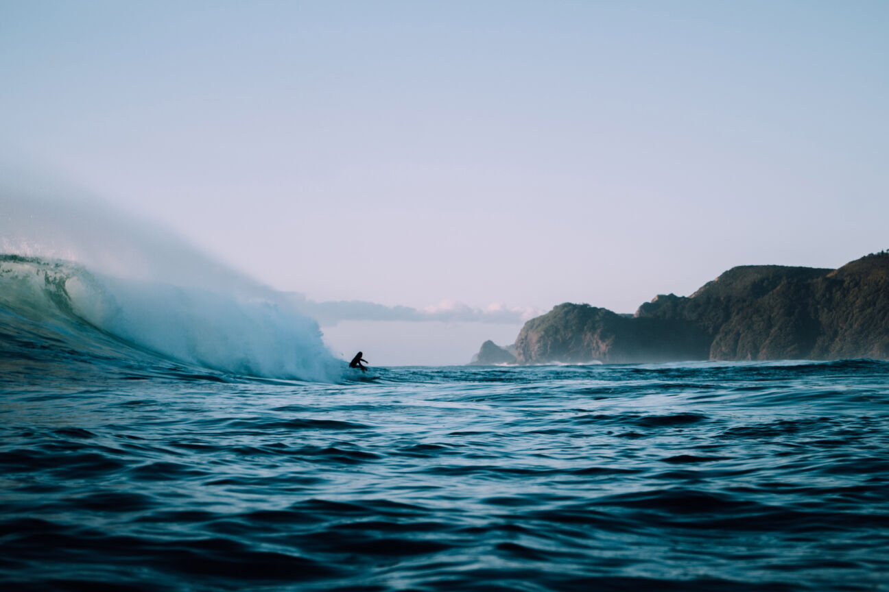 person surfs big wave off coast of beach in ocean