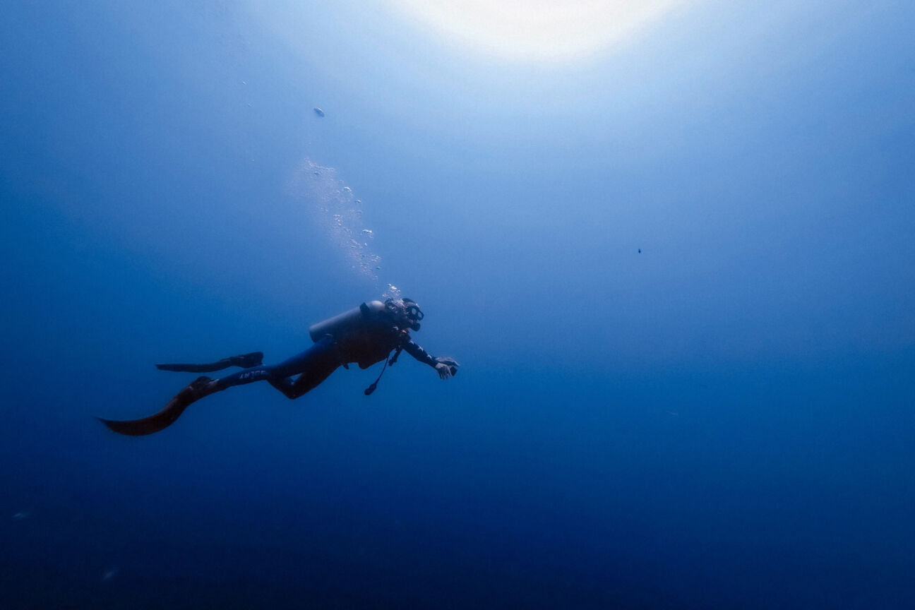 person dives to a reef in the ocean wearing full diving gear